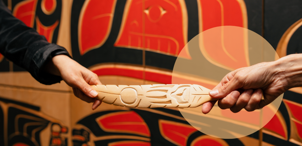 Two hands gently hold a carved wooden feather, symbolizing healing and remembrance for Truth and Reconciliation and Orange Shirt Day, a day to honour Indigenous children and survivors of residential schools.