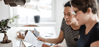 2 people hovered over a laptop at their kitchen table reviewing their bank statements and budget together.
