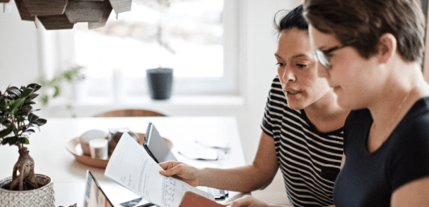 2 people hovered over a laptop at their kitchen table reviewing their bank statements and budget together.