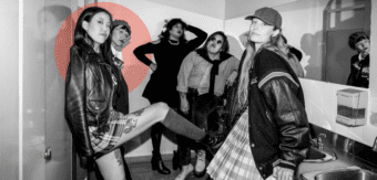 Amanda Kao leans against a wall in a bathroom with a group in punk-inspired outfits, reflecting boldness and community.