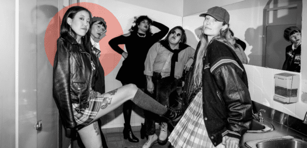 Amanda Kao leans against a wall in a bathroom with a group in punk-inspired outfits, reflecting boldness and community.
