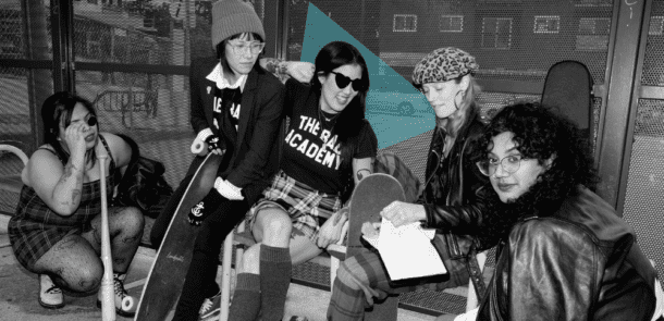 Black-and-white photo of Amanda Kao at the center with a group of women and gender-diverse individuals, some holding skateboards, wearing punk-inspired outfits. 'The Bad Academy' is printed on their shirts, reflecting creativity and community.