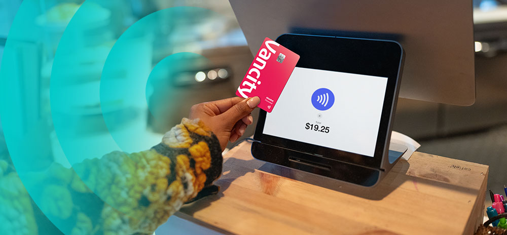 A person holding a credit card with a digital banking app open in front of a laptop.